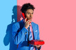 portrait of stylish african american man talking on retro telephone against pink and blue wall