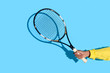 © LIGHTFIELD STUDIOS - Close-up view of male hand holding tennis racket on blue background