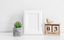 Empty Frame, Wooden Calendar And Cactus On Table Near White Wall