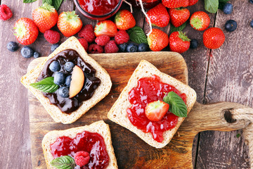 Wall Mural - Sandwiches with plum, strawberry jam and fresh fruits on wooden background