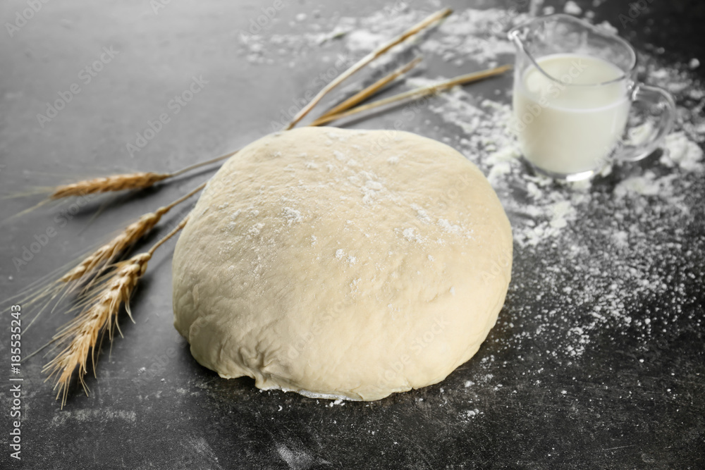 Fresh raw dough with jug of milk on table