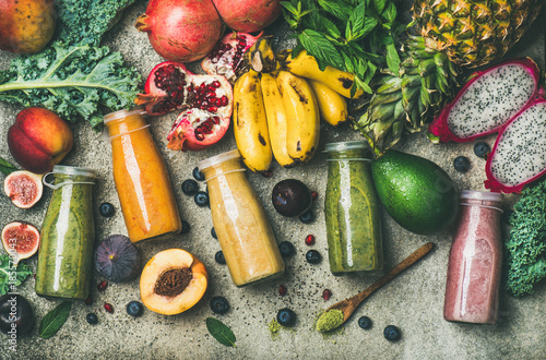 Fotografía Flat-lay of colorful smoothies in bottles with fresh tropical fruit and superfoods on concrete background, top view