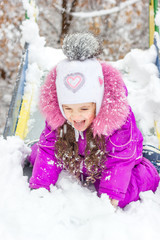 Kid girl on children slide at snowy winter day.