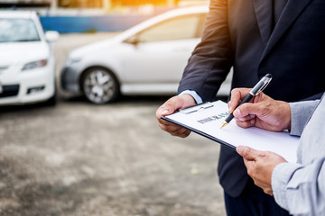 Car insurance agent send a pen to his customers sign the insurance form on clipboard while examining car after accident claim