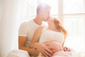 pregnant woman in a tulle skirt and her husband are sitting on the floor near a large window