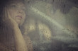 Sad woman looking through the window with rain drop in the car. Face of young female behind rain car window. Loneliness and depression concept. Psychology
