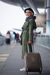 © Yakobchuk Olena - Ready to travel. Full length of positive senior woman wearing hat is standing outdoors with suitcase while looking at camera with joy. She is locating at international airport