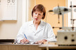 © rh2010 - Portrait of a senior woman ophthalmologist in unifrom sitting with different optical devices and eyeglasses during the work in the office