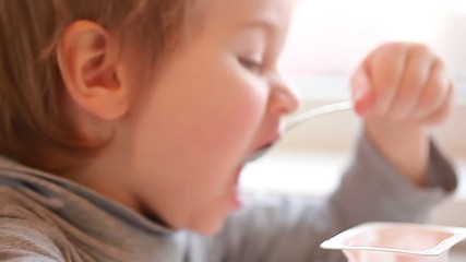 Wall Mural - video child eats yogurt with a spoon sitting at the table