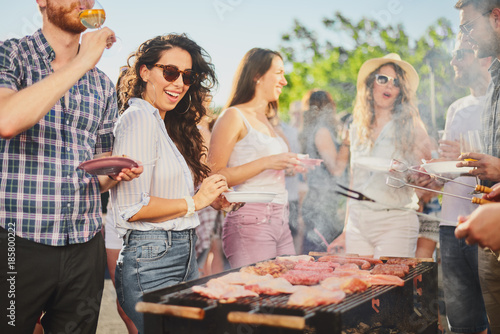 Plakat Grupa ludzi stojących wokół grilla, rozmowy, picia i jedzenia.