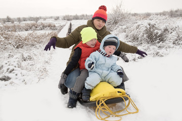 A happy family in colorful clothes posing in front of a photographer with a new yellow sled. Picturesque area with a bridge on the river. The concept of winter vacations, Christmas, New Year.