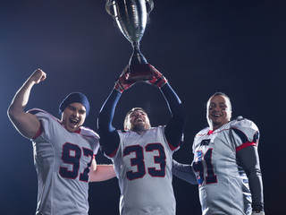 american football team with trophy celebrating victory