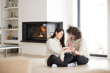Multiethnic Couple Using Tablet Computer In Front Of Fireplace
