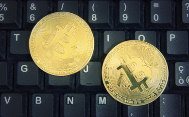 Two golden bitcoins on a computer keyboard.
