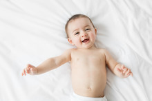 Overhead View Of Smiling Baby Girl Lying On The Bed 