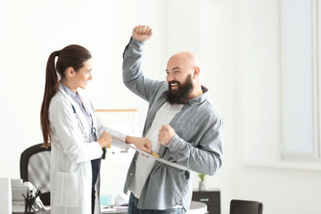 Wall Mural - Young female doctor measuring waist of overweight man with centimeter in clinic