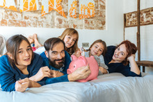 Mature Couple Relaxed At Home In Bed With Their Four Little Daughters Saving Money On The Piggy Bank.