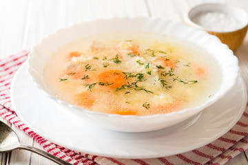 Wall Mural - Chicken soup with stelline pasta and carrot on white wooden table.