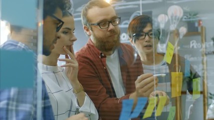 Diverse Team of Young Developers Brainstorming, They Have Discussion and Use Glass Board and Sticky Papers to Conceptualize Their New Plan. Shot on RED EPIC-W 8K Helium Cinema Camera.