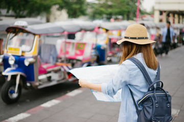 Wall Mural - Young woman traveler with sky blue backpack and hat looking the map with tuk tuk Thailand background from china town Bangkok. Traveling in Bangkok Thailand. Travel concept