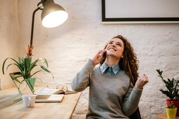 Wall Mural - Portrait of young woman talking on phone in modern office, celebrating success.