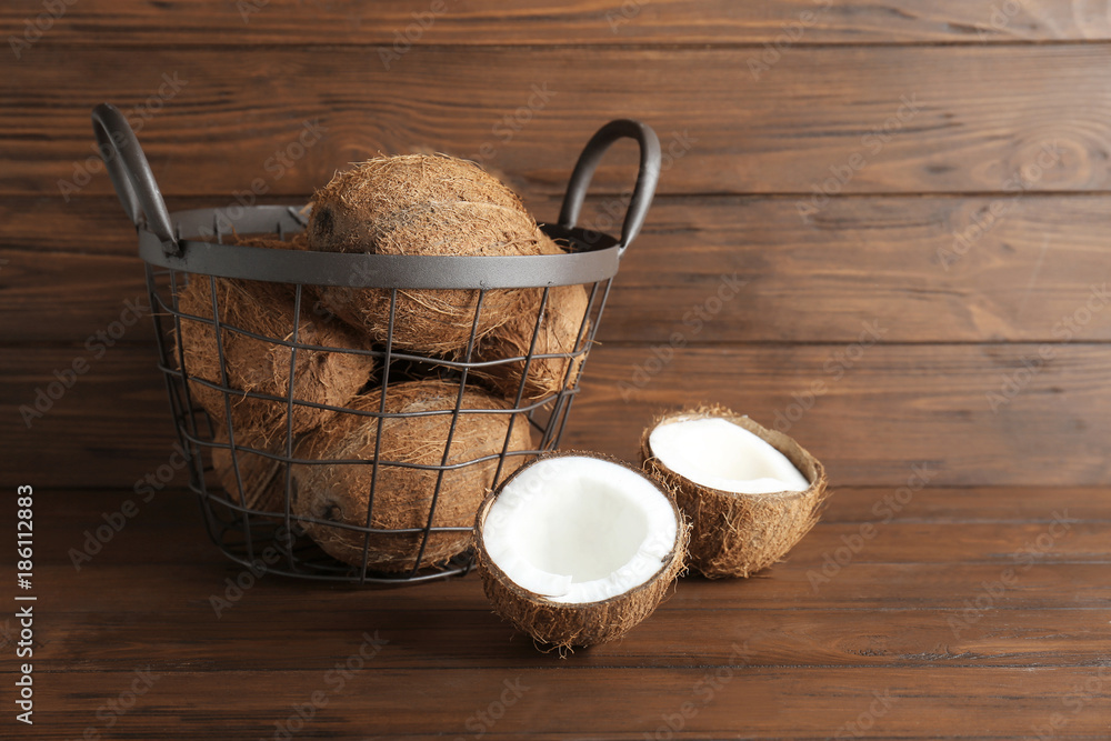 Metal basket with coconuts on wooden background
