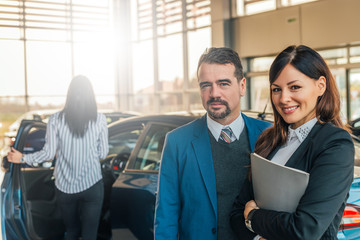 Portrait of two happy car sales consultants working inside vehicle showroom.