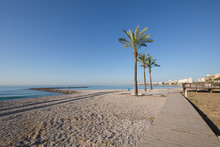 Landscape Els Terrers Beach, In Benicassim, Castellon, Valencia, Spain, Europe. Palm Trees, Wooden Walkway, Buildings, Blue Clear Sky And Mediterranean Sea
