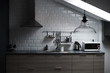 Kitchen in a loft style with concrete and brick walls and tiles, a sink, vent, microwave, teapot and a modern lamp.
