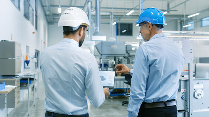 Wall Mural - Back View of the Head of the Project Holds Laptop and Discussing Product Details with Chief Engineer while They Walk Through Modern Factory.