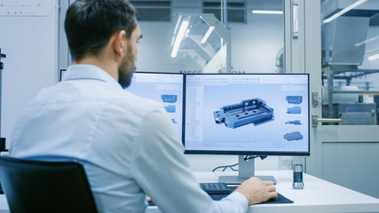engineer/ technician working on a personal computer with two displays, he's designing new component 