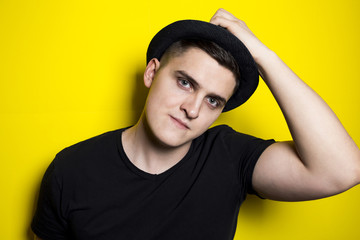 young attractive man with a modern haircut in a fashionable black hat on the back of the head and black t-shirt on a bright contrasting yellow background