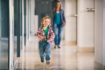 Little boy running in the shopping center with his mom on background.