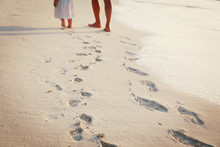 Mother And Daughter Walking On Beach Leaving Footprint In Sand