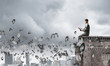 © adam121 - Man on roof edge send message with smartphone and symbols flying around