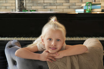 Poster - Adorable little girl in armchair near piano indoors