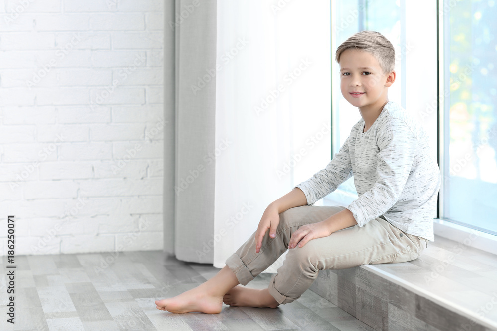 Cute fashionable boy sitting on windowsill
