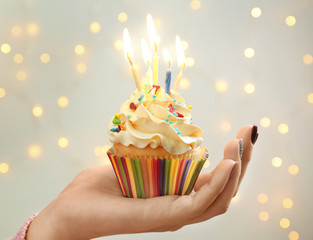 Poster - Woman holding birthday cupcake with candles against blurred lights, closeup