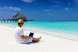 Geschäftsmann sitzt mit seinem Laptop am tropischen Strand und arbeitet