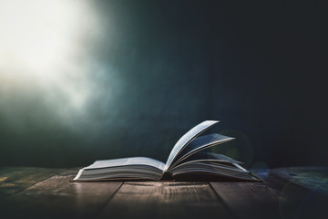 open bible with a light coming from above on a wooden desk