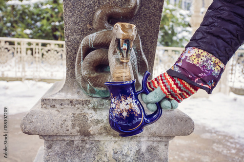 Fotografie, Obraz Hand filling a cup with therapeutic mineral water at a natural hot spring in Karlovy Vary during winter time, Czech Republic