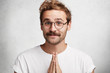 © wayhome.studio  - Funny bearded male with hands pressed together, looks innconetly, asks his girlfriend for forgiveness, promises for imporovement, looks with cheerful expression. Unshaven hipster gestures indoor