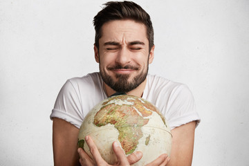 this is my palnet! pleased emotional bearded young male closes eyes with enjoyment as embraces globe