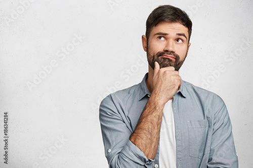 Fotografía Thoughtful man with stubble looks pensively upwards, has pleasant dreams as plan