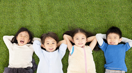Wall Mural - happy boys and girls lying on green grass.