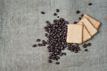  The background of a gray cloth made of old and coarse burlap, on which lies a certain amount of brown coffee beans with a yellow rectangular biscuit