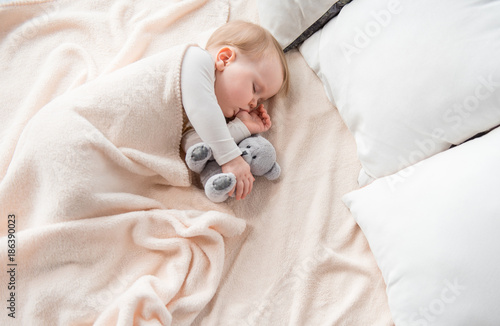 Foto Top view of peaceful baby lying at sheets and sucking her finger