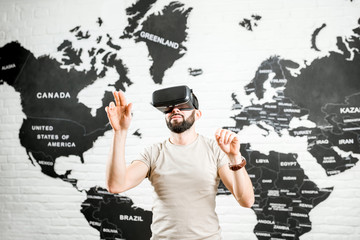 Man using virtual reality glasses sitting indoors with world map on the background