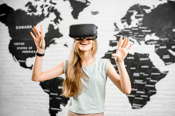 Young woman using virtual reality glasses sitting indoors with world map on the background