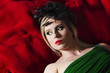 © grufnar - portrait of a blonde woman wearing makeup and a black retro hat lying on a red blanket